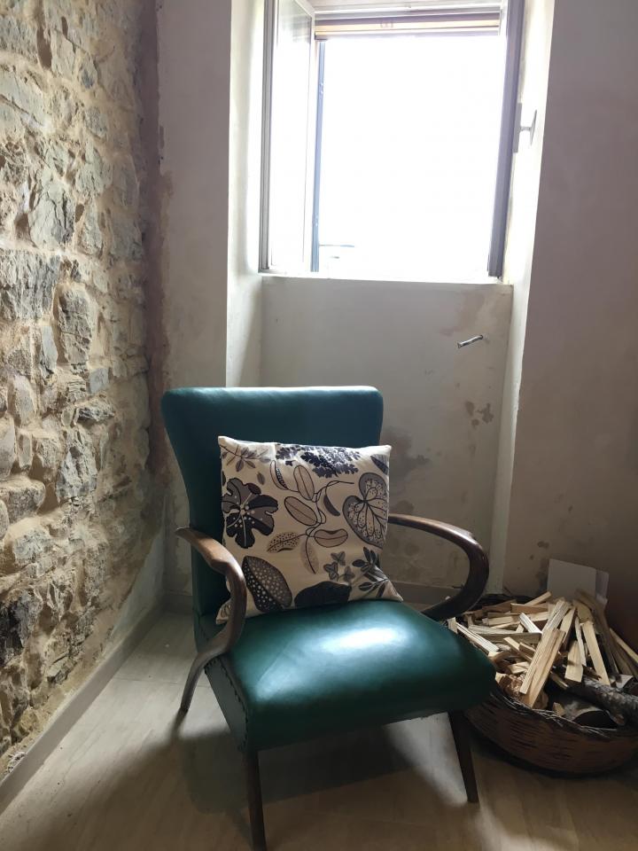 Green retro 50s armchair in a sunlit window by a basket of logs