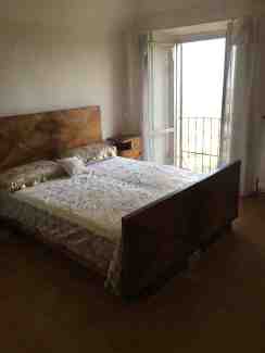 An art deco wooden bed with gold and white bedding by a bright open window