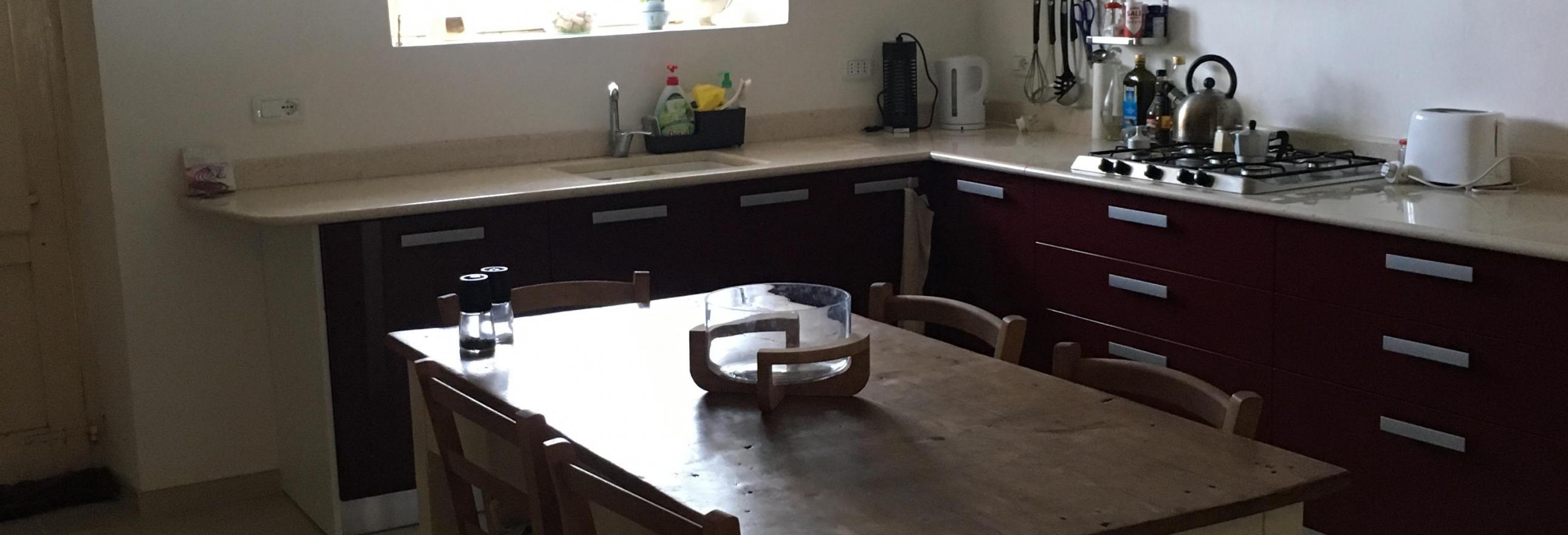 View of kitchen table with worktops and shiny deep red cabinets in the background