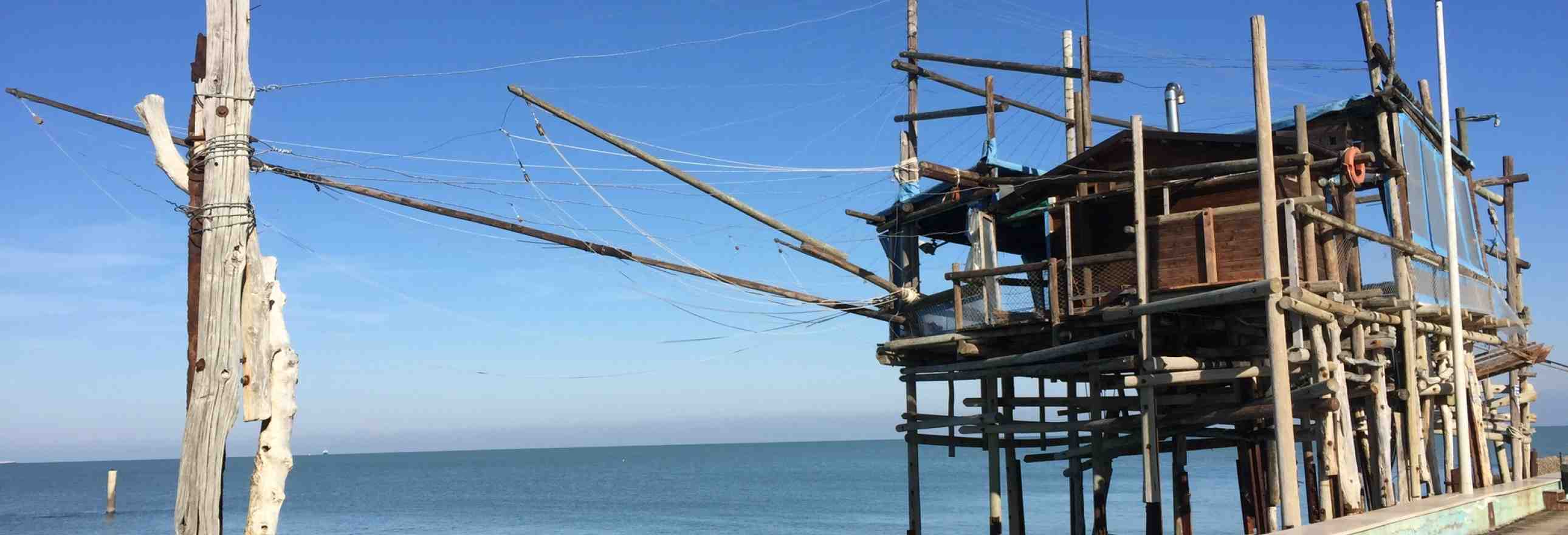 A spindly wooden fishing structure just off the beach against a bright blue sky